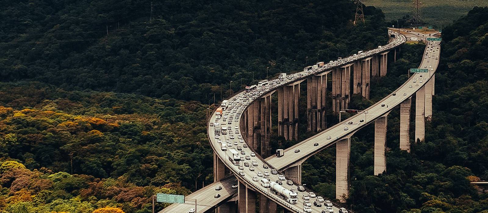Rodovia em viaduto serpenteando pela mata, em São Paulo.