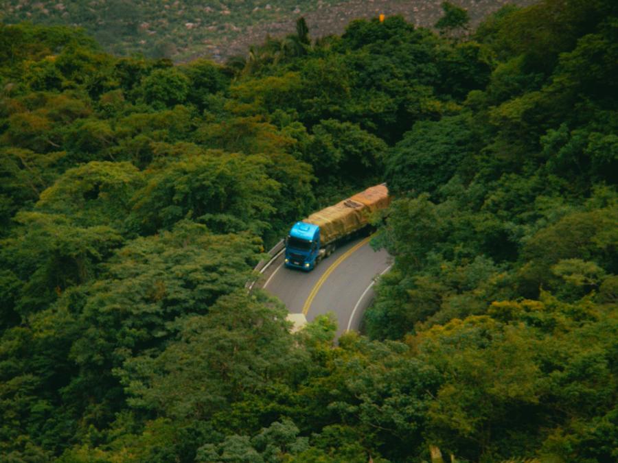 Caminhão numa estrada em curva no meio da mata, na serra do Ceará, visto de cima.